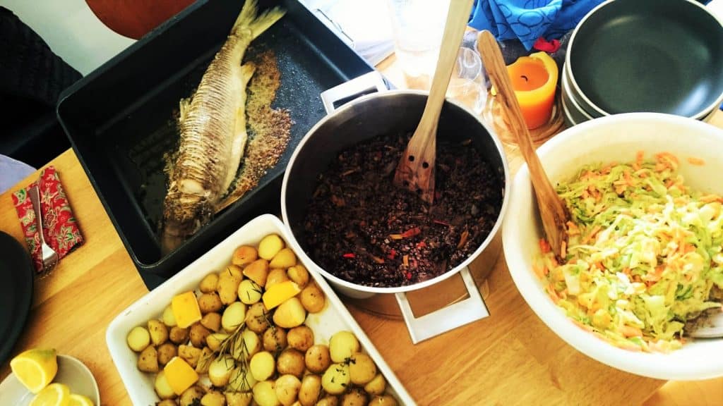 Eine Tafel voller Essen und ein Fisch darauf, präsentiert bei einem Fischkochkurs.