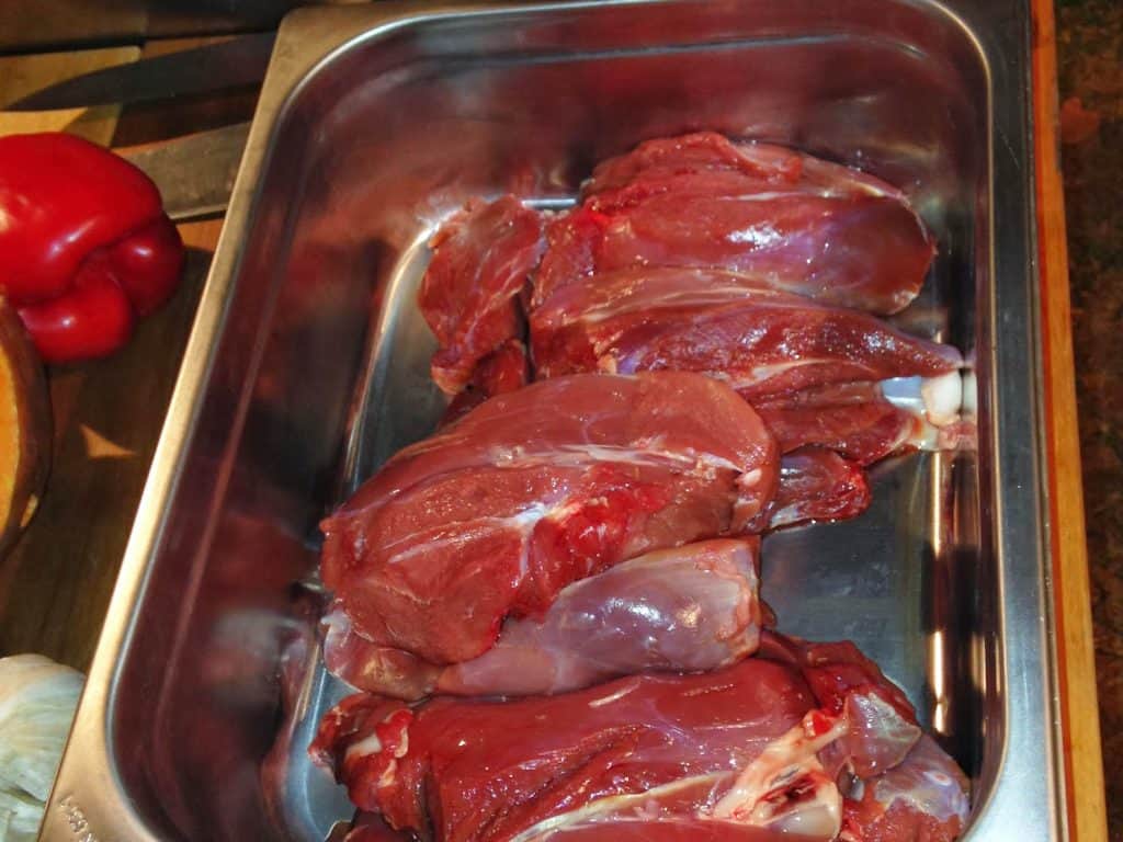 Auf einem Holztisch steht ein Tablett mit rohem Wildfleisch, vorbereitet für einen Kochkurs.