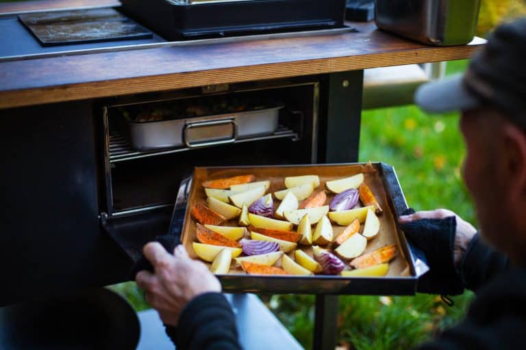 Ein Mann hält ein Tablett mit veganem Essen in einem Ofen im Freien.