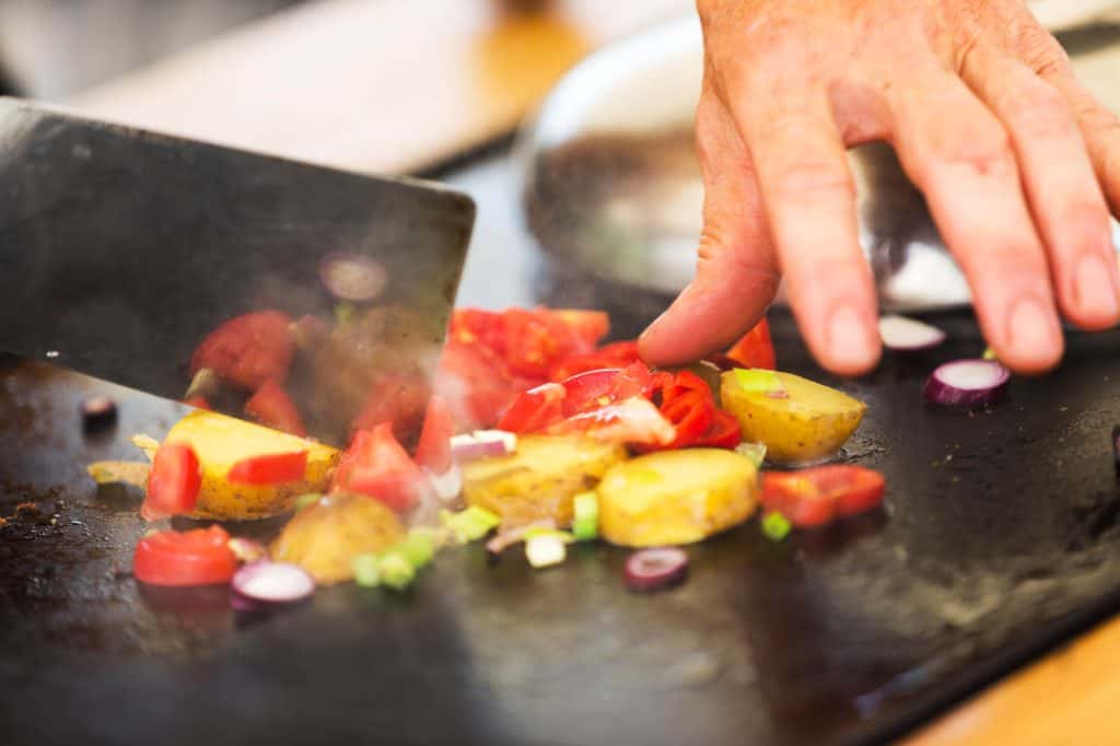 Eine Person schneidet in einem veganen Kochkurs Gemüse in einer Pfanne.