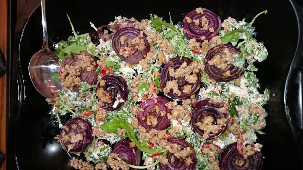 Ein Teller mit roten Zwiebeln und Gemüse mit einem Löffel, perfekt für einen veganen Kochkurs.