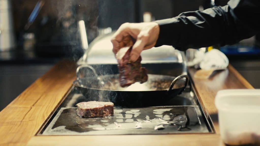 Ein Mann bereitet bei einem Kochkurs ein Steak in einer Bratpfanne zu.